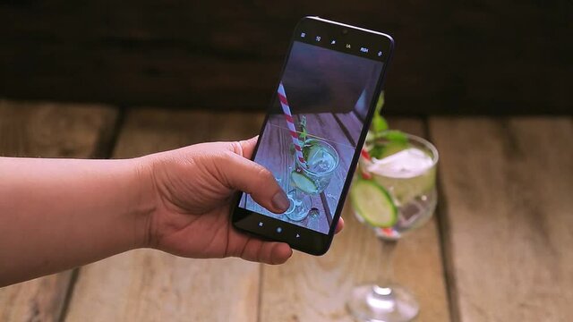 Cocktail with mint cucumber and lemon in a glass female hand takes a picture on a smartphone