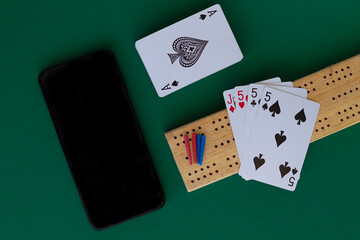 cribbage wooden games.playing card and cribbage board with black phone on the green.playing cards with blue deck on the table. combination of cards on a casino desk background with copy space.top view