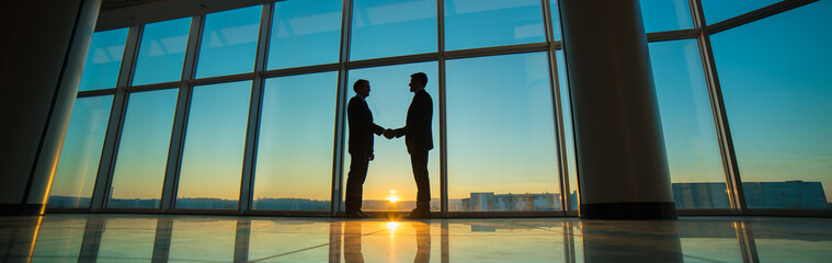 Fototapeta na wymiar The two men handshake in the office on the sunset background