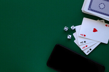 online poker games. four aces with dice and phone in casino. playing cards with blue deck on the green table. combination of cards on a green casino desk background with copy space. top view