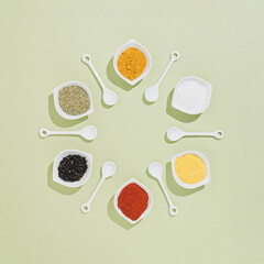 Creative and modern layout made with kitchen spices in small  white bowls,  on pastel green background. Flat lay. Minimal concept.