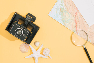 Summer travel flet lay background, made with different shells, old camera, magnifier, map and white envelope .Pastel yellow background. © Lelija