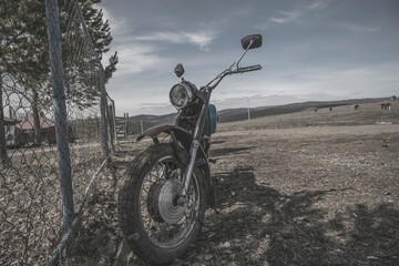 An old abandoned motorcycle stands by the fence. Beautiful nature. Abandoned old technology. Abandoned bike