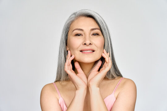 Portrait of gorgeous beautiful middle aged mature asian woman, senior older 50 year lady looking at camera touching her face isolated on white. Ads of lifting anti wrinkle skin care, spa.