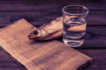 Shot of vodka with a stockfish and a piece of cloth on an old wooden table. Close up view