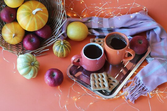 Thanksgiving day, two cups of coffee, meringues, pumpkins, apples, leaves, warm blanket on an orange background, the concept of home comfort, family holidays, autumn season 