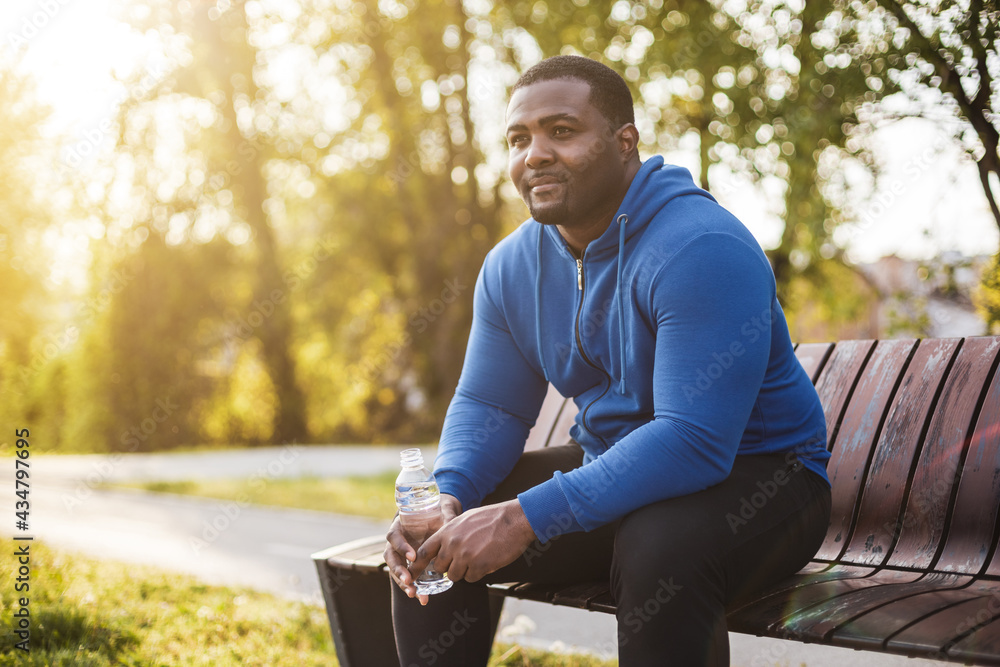 Wall mural man resting on bench after exercise and drinking water .