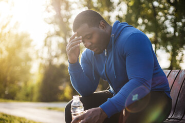 Exhausted man after exercise drinking water while sitting on bench.