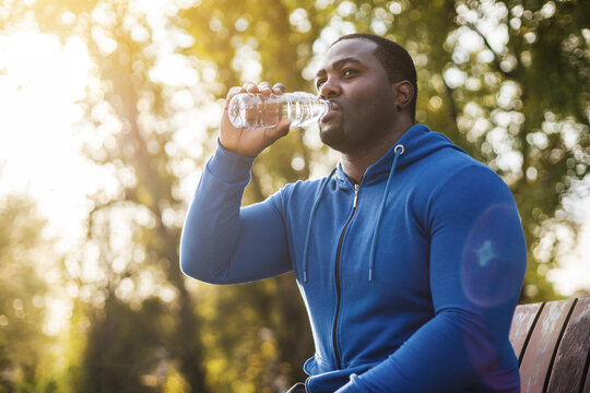 Man Resting On Bench After Exercise And  Drinking Water .