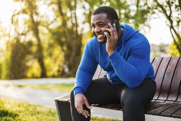 Fototapeta premium Man using mobile phone while resting after exercise on bench.