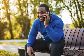 Fototapeta premium Man using mobile phone while resting after exercise on bench.