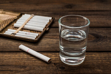 Shot of vodka with cigarette and cigarette case on an old wooden table. Close up view - obrazy, fototapety, plakaty