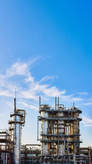 Old distillation column towers and reactors under blue evening sky background at chemical plant. Exterior of silver metal rusty enterprise 16x9 vertical with copyspace.