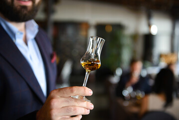 A glass with wiskey in hand of man with blurred background. Concept of whiskey tasting.