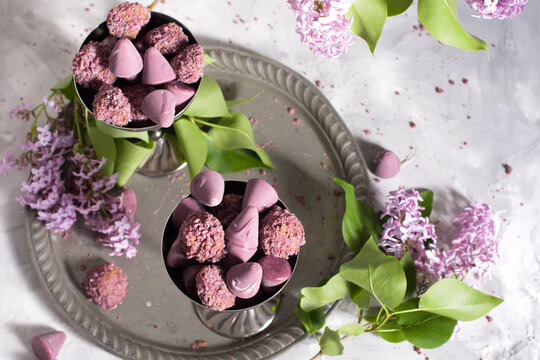 Belgian sweets cuberdon and pralines in silver glasses, spring still life with lilac flowers, flat lay