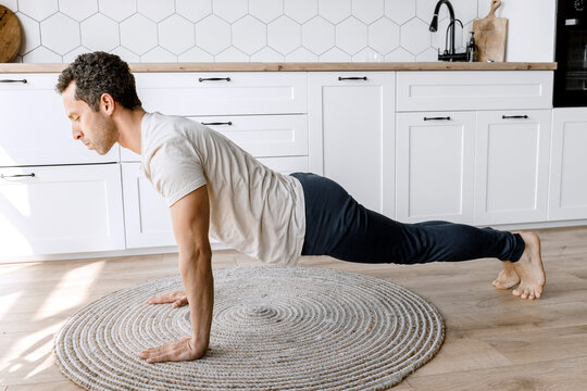 Home Workout. Sporty man working hard and making push up exercise on the floor of his kitchen before Zoom conference. Sport and healthy lifestyle concept.