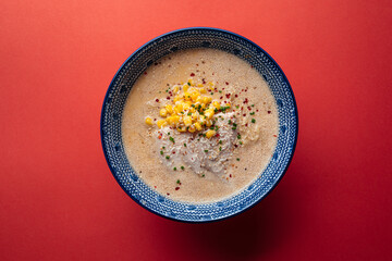 Bowl of cheese ramen noodle soup with corn on pink background