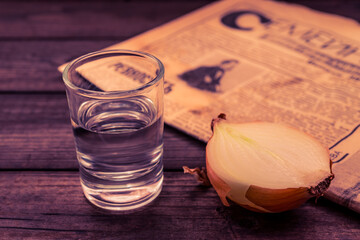 Shot of vodka with  newspaper and onion on an old wooden table. Close up view