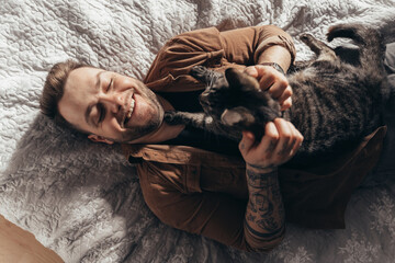 Man laughing and stroking his striped cat while spending time with him at bedroom