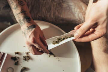 Man putting marijuana at special paper while the rolling a hand rolled cigarette