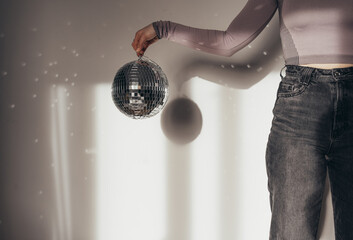 Unrecognizable woman holding disco ball in front of the white wall