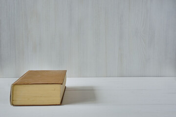 Old brown book lies on a white wooden table on a light wood background withcopy space for text. The concept of study, reading, self-development, bookstores.