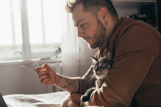 Man smoking cannabis and spending time with his cat while watching something