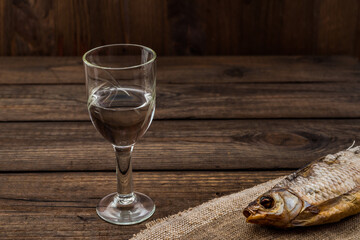 Shot of vodka with a stockfish and a piece of cloth on an old wooden table. Angle view