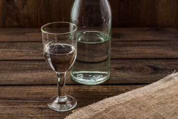 Glass of vodka and bottle with piece of cloth on an old wooden table. Angle view, focus on the glass of vodka