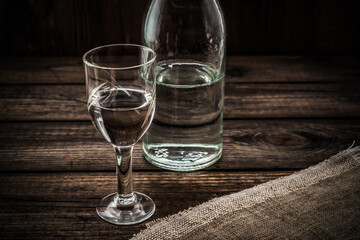 Glass of vodka and bottle with piece of cloth on an old wooden table. Angle view, focus on the glass of vodka
