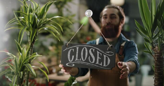 Flower shop employee flipping sign on glass entrance door from closed to opened, starting workday of greenhouse. Small business people 4k footage