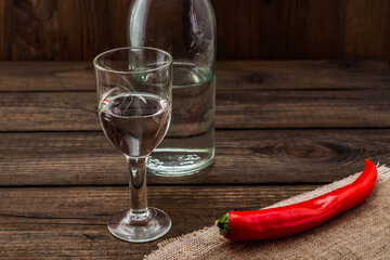 Glass of vodka and bottle with piece of cloth and cayenne pepper on an old wooden table. Angle view