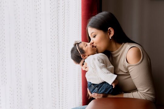 Hispanic mom kissing her newborn baby while holding him - latin mother and daughter at home.