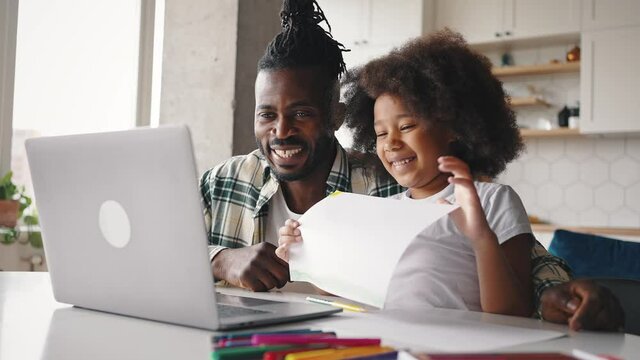African american girl and her daddy video calling to family, daughter showing picture to laptop, proud man embracing her