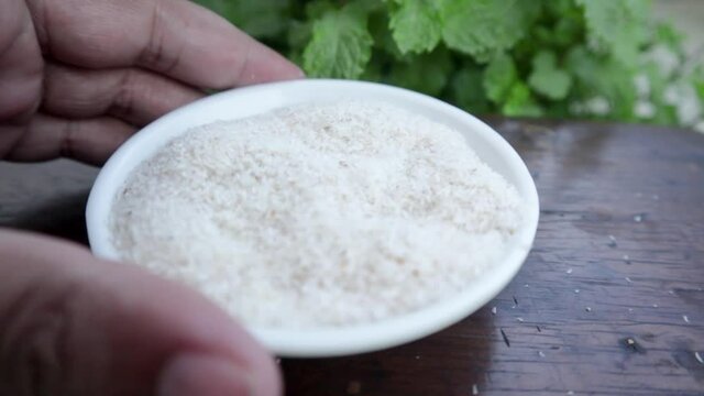 Showing small plastic bowl of Psyllium husks with hand