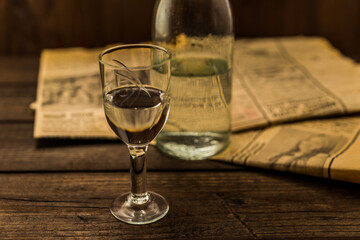Glass of vodka with bottle and newspaper on an old wooden table. Angle view, shallow depth of field, focus on the glass of vodka