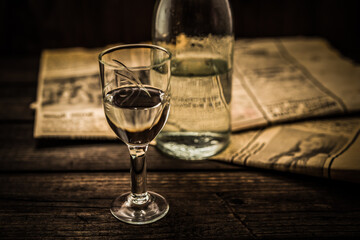 Glass of vodka with bottle and newspaper on an old wooden table. Angle view, shallow depth of field, focus on the glass of vodka