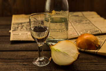 Glass of vodka with  newspaper and onion with bottle on an old wooden table. Angle view, shallow depth of field
