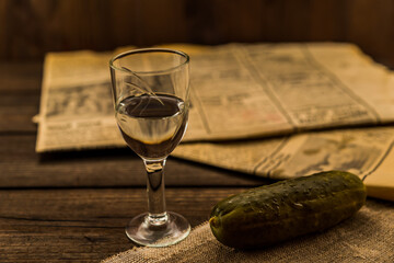 Glass of vodka with  newspaper and pickled cucumber with canvas on an old wooden table. Angle view, shallow depth of field
