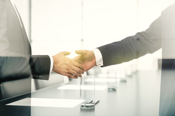 Handshake of two businessmen on boardroom interior background, deal and trading concept. Multiexposure
