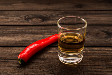 Glass of tequila with cayenne pepper on an old wooden table. Close up view