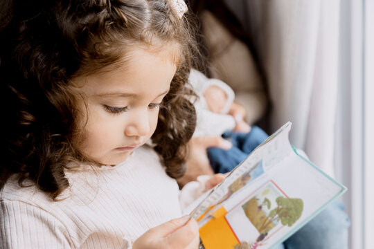 Hispanic toddler girl watching a picture book with her mom-Little girl learning to read
