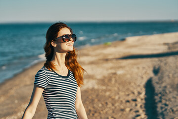 beautiful woman in a t-shirt and glasses on the beach near the sea in the mountains