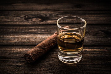 Glass of tequila with cuban cigar on an old wooden table. Close up view