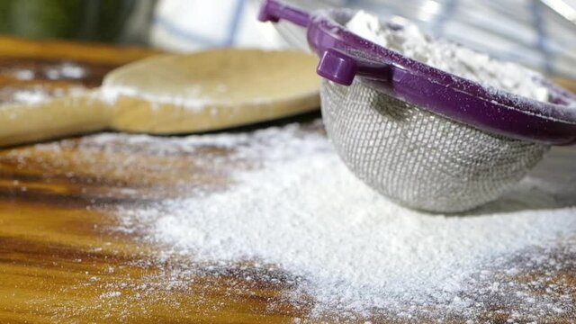 A sifter full of flour falling onto a cutting board in super slow motion
