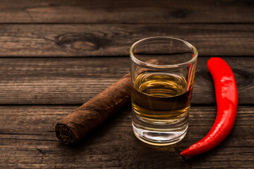 Glass of tequila with cayenne pepper and cuban cigar on an old wooden table. Close up view