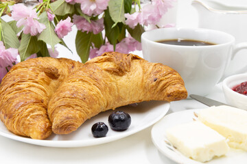 A cup of coffee and croissants with jam and butter. A breakfast idea.