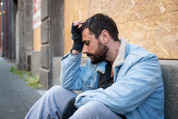 Young hungry unemployed sick depressed homeless homeless man sitting on the street in the city begging for money waiting to earn something to buy food to eat, social documentary concept