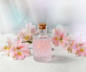 Beautiful perfume or aromatic oil glass with flowers over light background. Close up composition for spa, aromatherapy or massage. Relaxation. Wellness. Natural organic cosmetics.