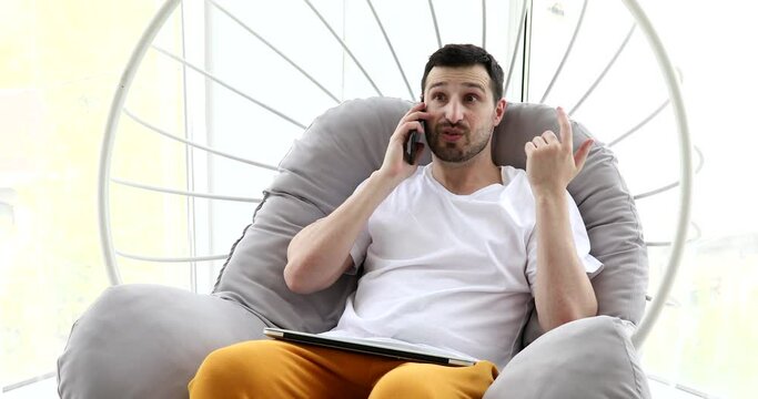 Happy Young Man Uses Smartphone while Sitting on a Sofa at Home.